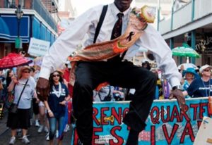 A photo of a bandleader with colorful sash jumping in the air in the French Quarter of New Orleans.