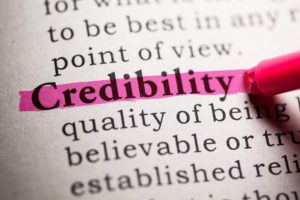 Close up of a definition of credibility with a pink highlighter highlighting the word credibility.